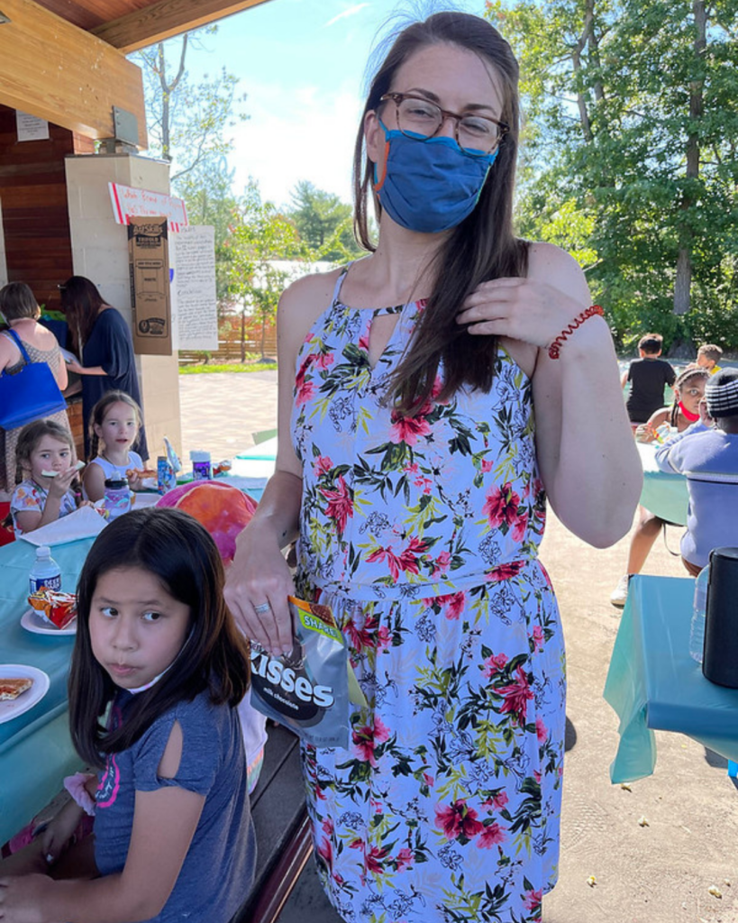 A woman outside with children eating at picnic tables nearby.