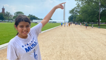 An image of a girl smiling and pointing with the Washington Monument in the background.