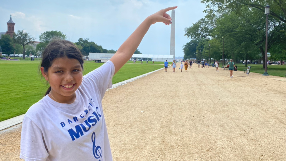 An image of a girl smiling and pointing with the Washington Monument in the background.