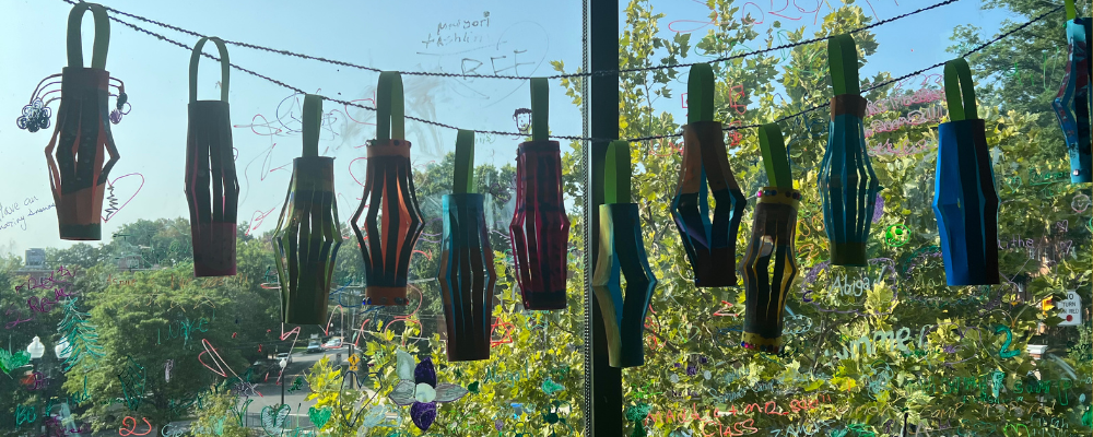 Six colorful paper lanterns hanging in front of a window