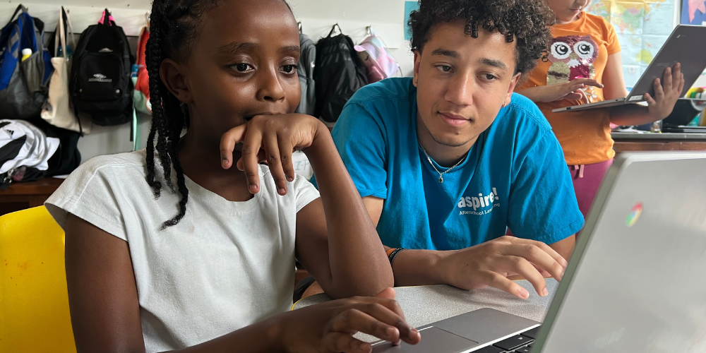 A young girl sitting in front of a computer, and a man sitting next to her, looking at the screen.