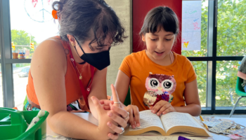 A young woman and a girl reading together at a table