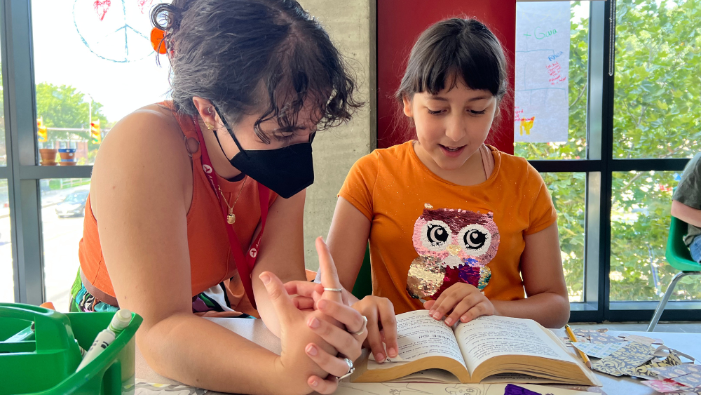 A young woman and a girl reading together at a table