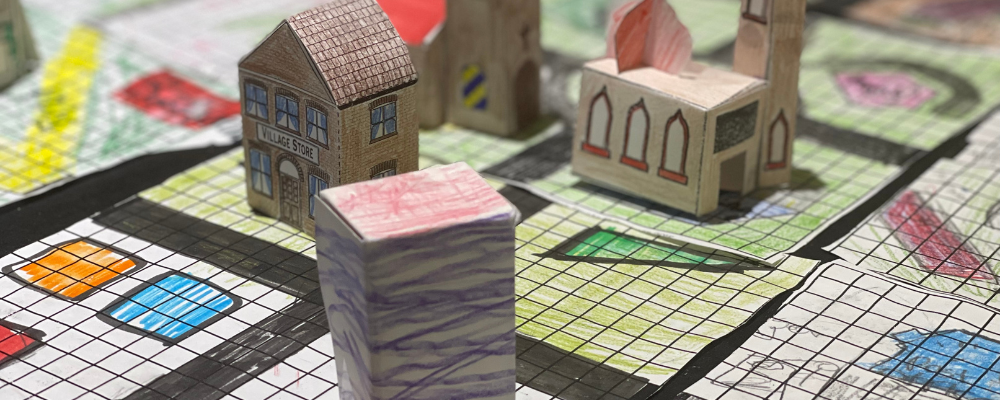 A photo of tiny buildings made out of paper laid out on a paper grid.