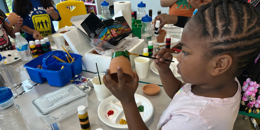 A photo of a young girl painting a small pot green