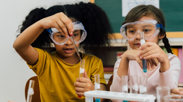 A photo of two young girls wearing science goggles and holding beakers