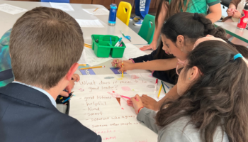 A group of students and an adult writing on a large sheet of white paper