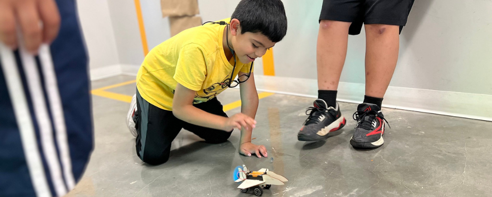 A photo of a boy kneeling by a small electric car that he made