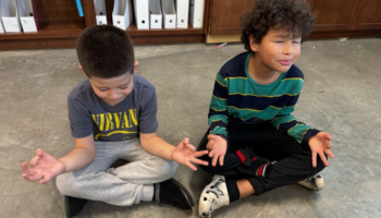 A photo of two boys sitting on the floor and meditating