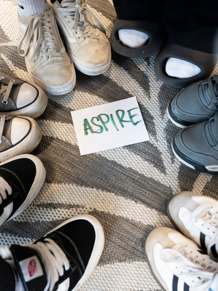 A piece of paper that reads "Aspire" on the ground with feet in a circle around it