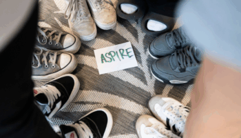 A piece of paper that reads "Aspire" on the ground with feet in a circle around it