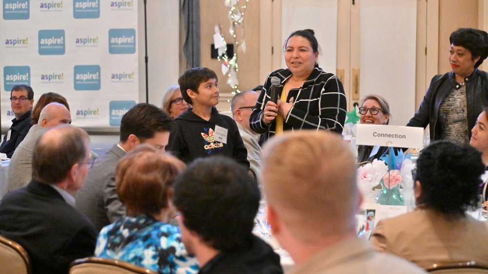 A woman standing up and speaking in a crowded room