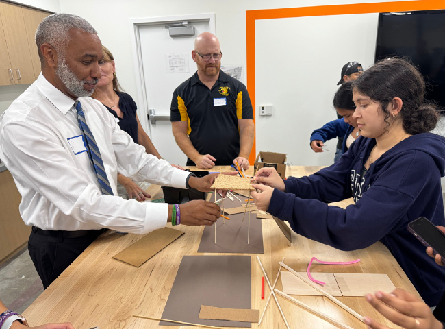 A student working on an engineering project with the assistance of adults