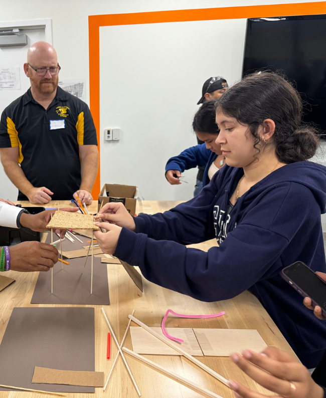 A student working on an engineering project with the assistance of adults