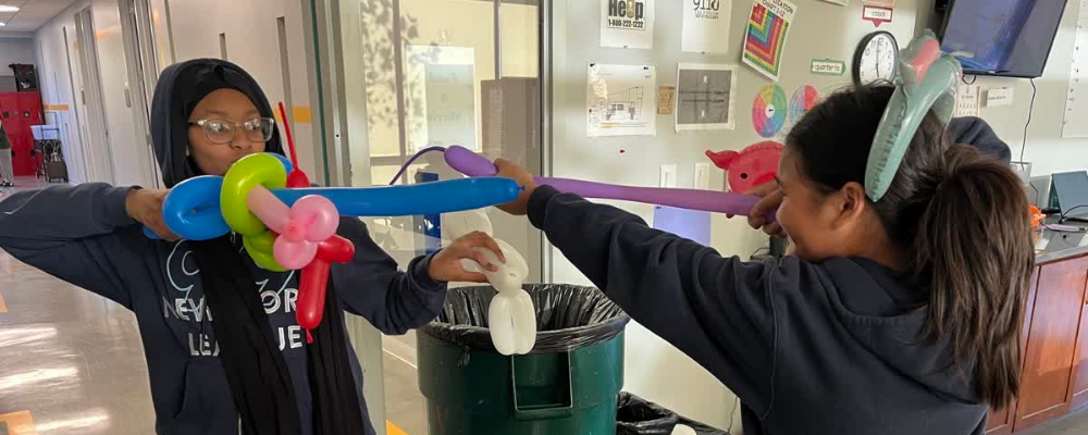 A photo of two students playing with balloon swords